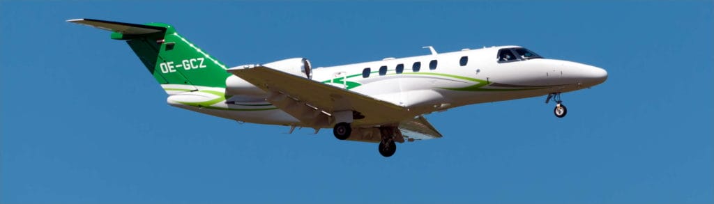 Ein weiß-grünes Privatflugzeug mit der Kennung "OE-GCZ" fliegt am blauen Himmel, Fahrwerk ausgefahren für die Landung.