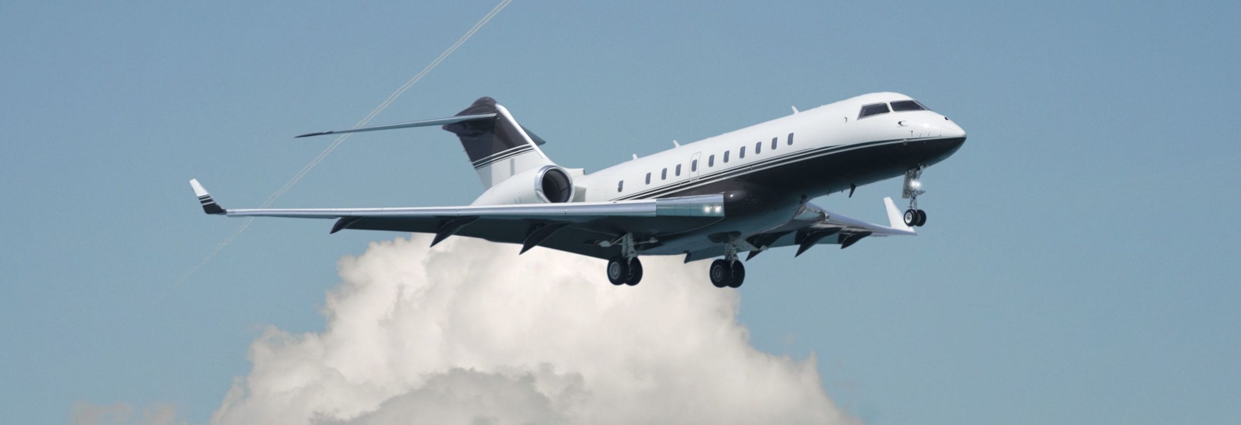 Ein weißes Flugzeug fliegt durch die Luft, mit einem klaren blauen Himmel und großen Wolken im Hintergrund.