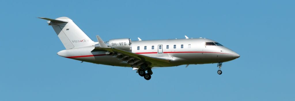 Ein silbernes Flugzeug fliegt am blauen Himmel. Es trägt die Aufschrift "VISTAJET" und erkenntlich ist die Registrierungsnummer "9H-VFG".