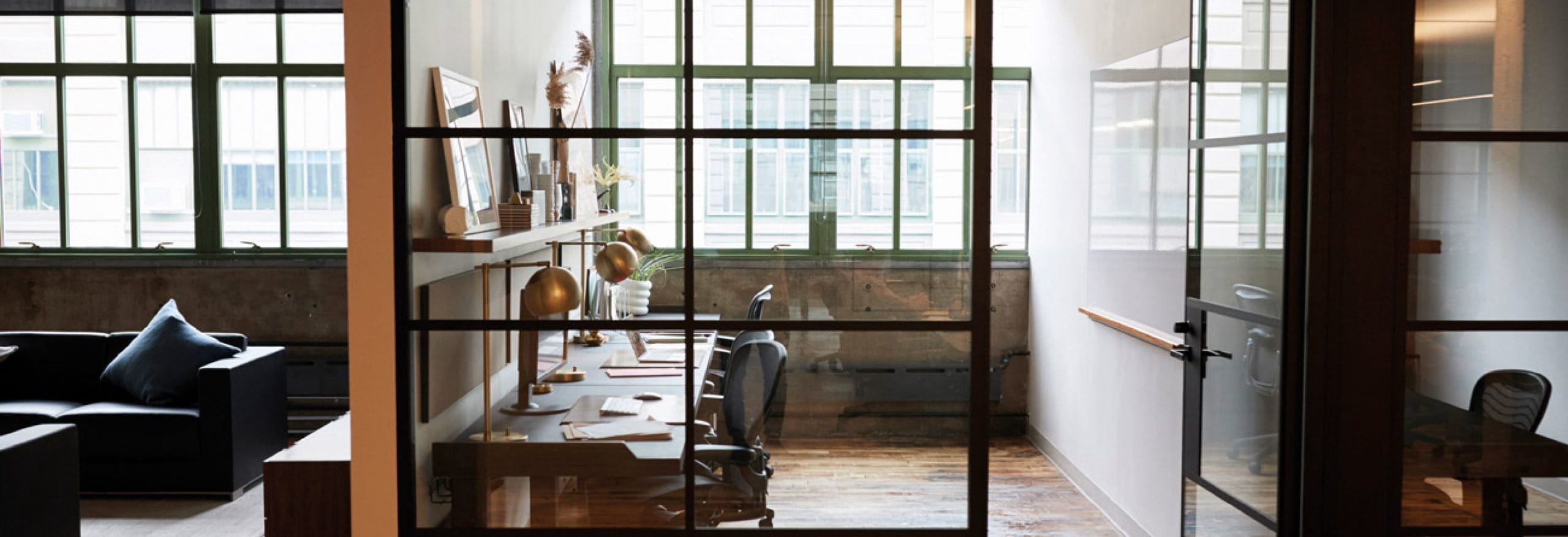 Büro mit Glaswänden: Zwei Schreibtische mit Lampen vor großen Fenstern. Moderne, stilvolle Einrichtung in einem hellen und offenen Raum.