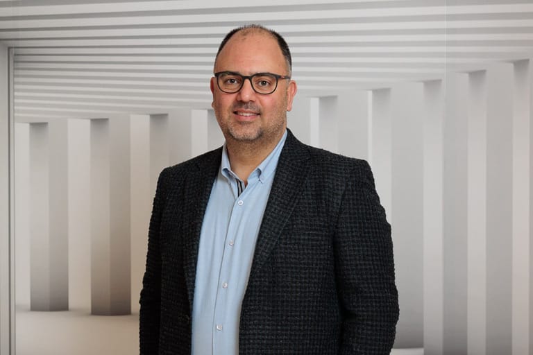 Darstellung von Serkan Topcu, erneut frontal abgebildet, mit leicht verändertem Gesichtsausdruck im gleichen Studiohintergrund.