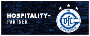 Logo VfL Gummersbach – Symbol mit Schriftzug "HOSPITALITY-PARTNER" auf strukturierter, dunkelblauer Ziegelwand. Drei Sterne schweben darüber.