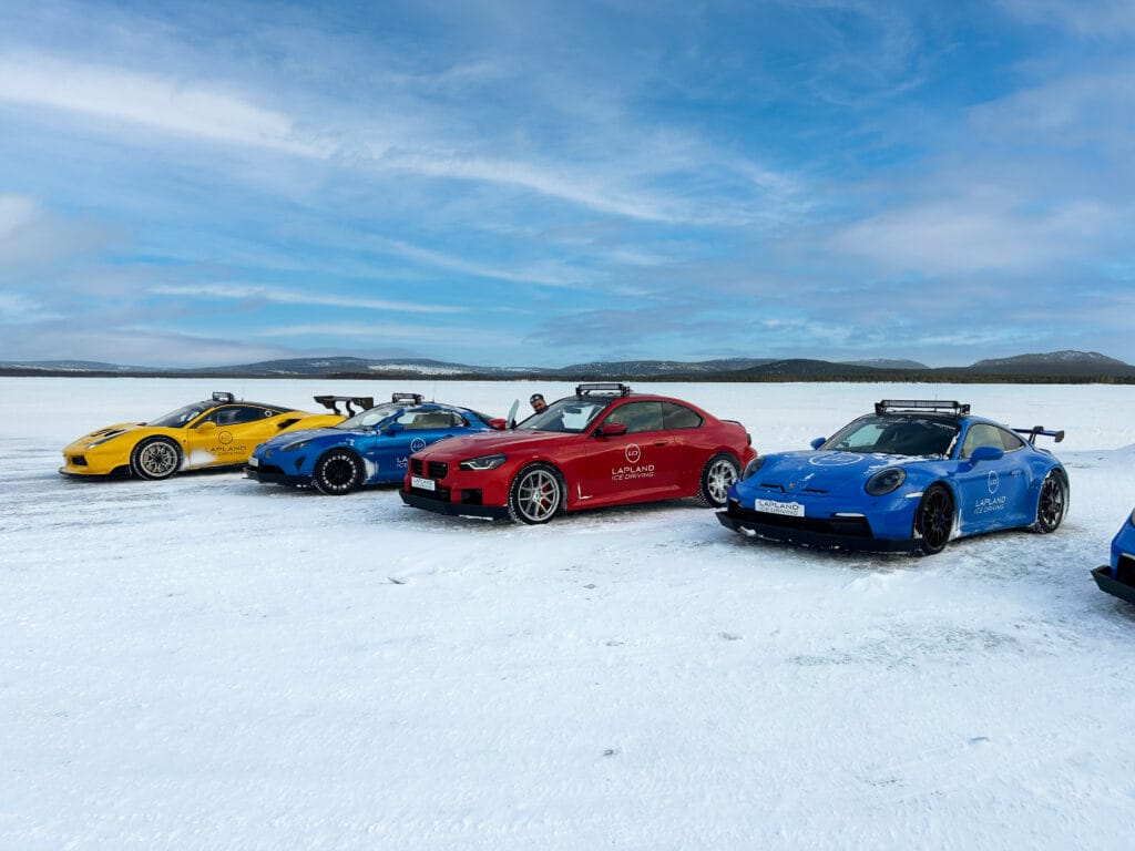 Vier Sportwagen stehen auf einem verschneiten Feld, umgeben von der winterlichen Landschaft Arvidsjaur.